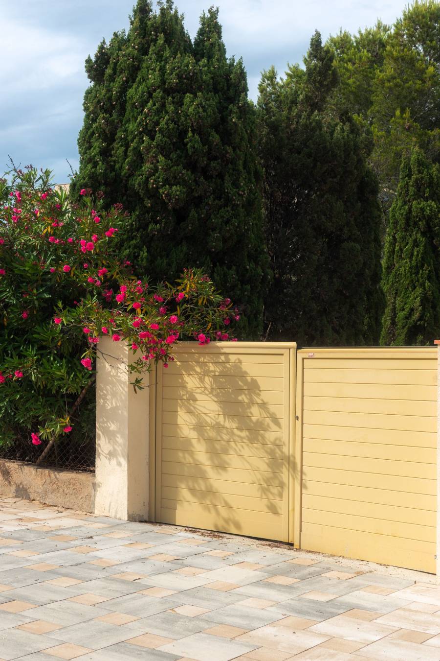 Le choix du pvc pour votre portail portail en pvc beige clair entouré de fleurs et d'arbustes de couleurs roses foncées