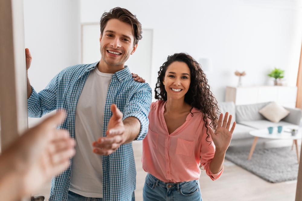 Déroulement pose fenêtre avec RSM Rénovation Portrait d'un couple joyeux invitant les invités à entrer à la maison, jeune homme et femme heureux debout à la porte d'un appartement moderne, regardant dehors, homme serrant la main, rencontrant RSM Rénovation lors du premier rendez-vous