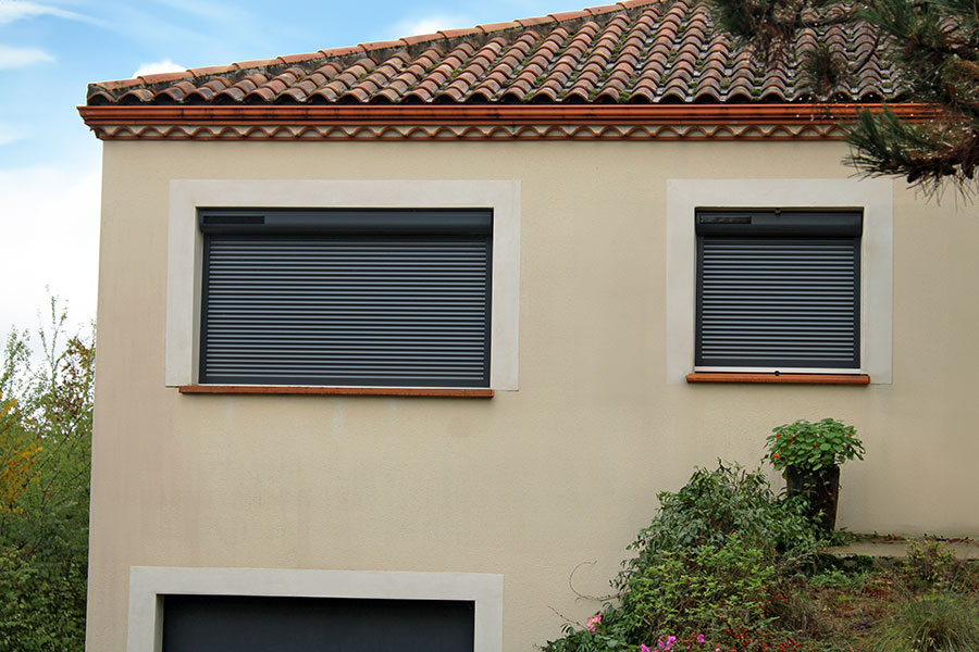 Fonctionnement et consommation des volets roulants électriques Vue sur la façade d'une maison beige avec des volets roulants électriques anthraciques
